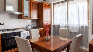Una cocina con estufa, horno y lavadora, armarios de madera y una mesa de comedor con sillas.