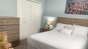 A bedroom with a bed, a nightstand, a dresser, a closet, and a cityscape painting on the wall. - Cozy Basement Suite close to Downtown (Edmonton)