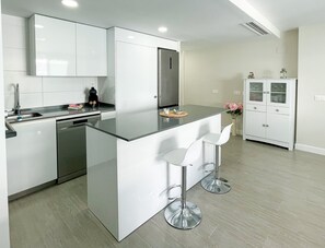 Een moderne keuken met witte kasten, een roestvrijstalen koelkast en een centraal eiland met barstoelen.