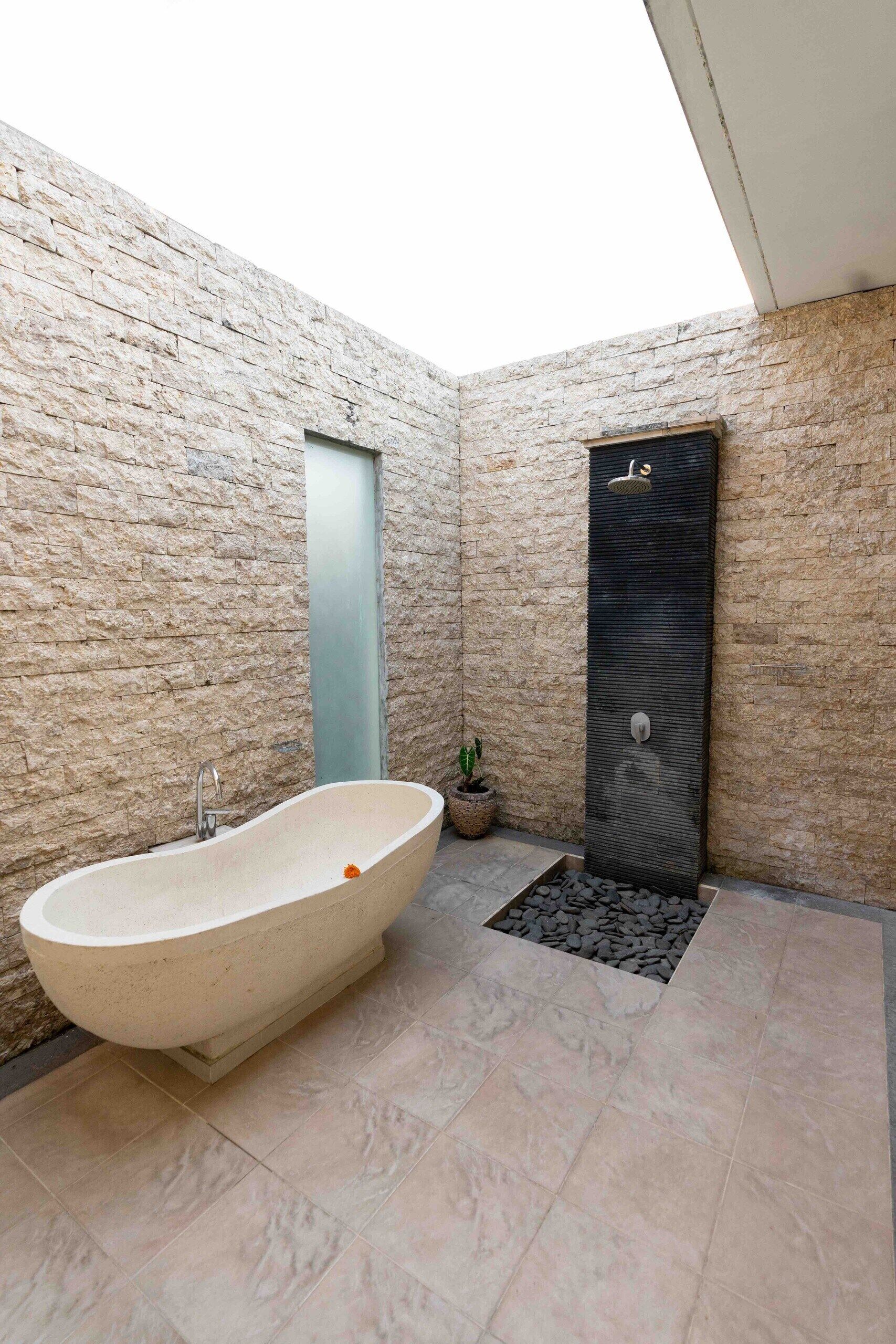A modern bathroom with a freestanding bathtub, a vertical water feature, and a potted plant.