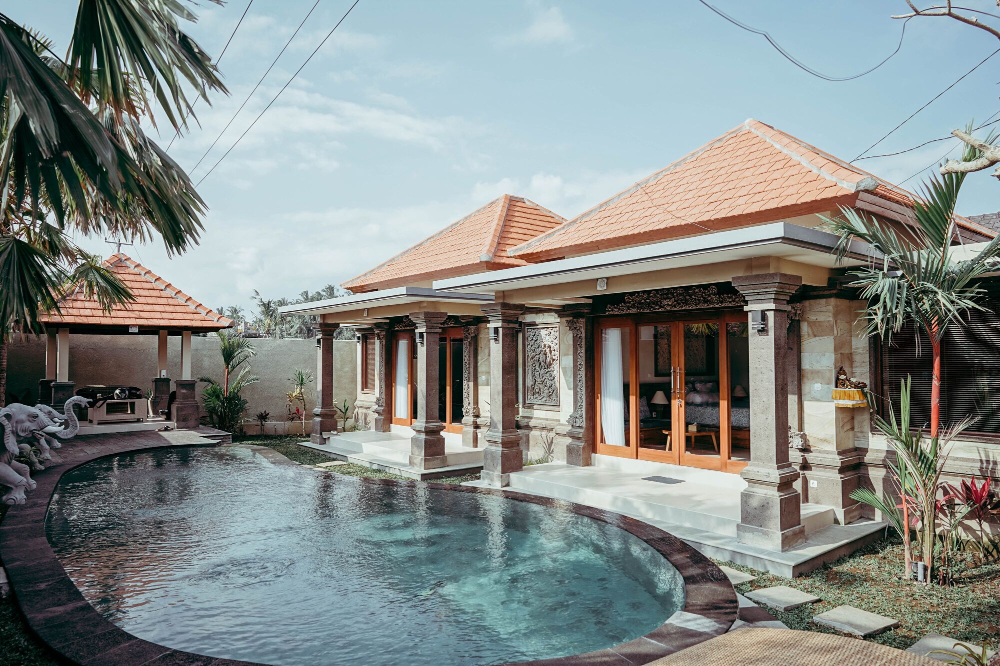 A poolside area with a swimming pool, a covered seating area, and a building with a tiled roof and columns.