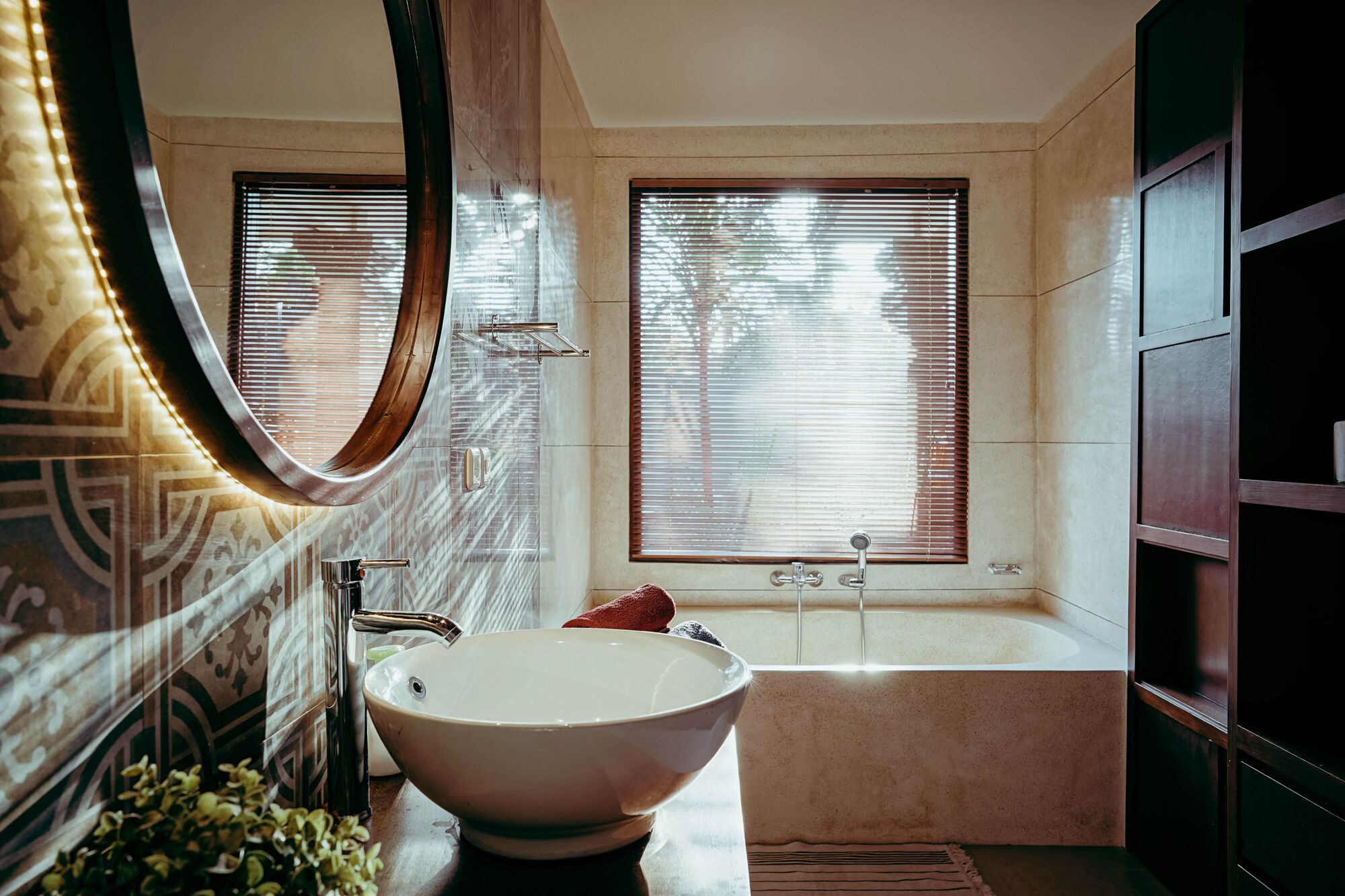 A bathroom with a large oval sink, a bathtub, and a window with blinds.