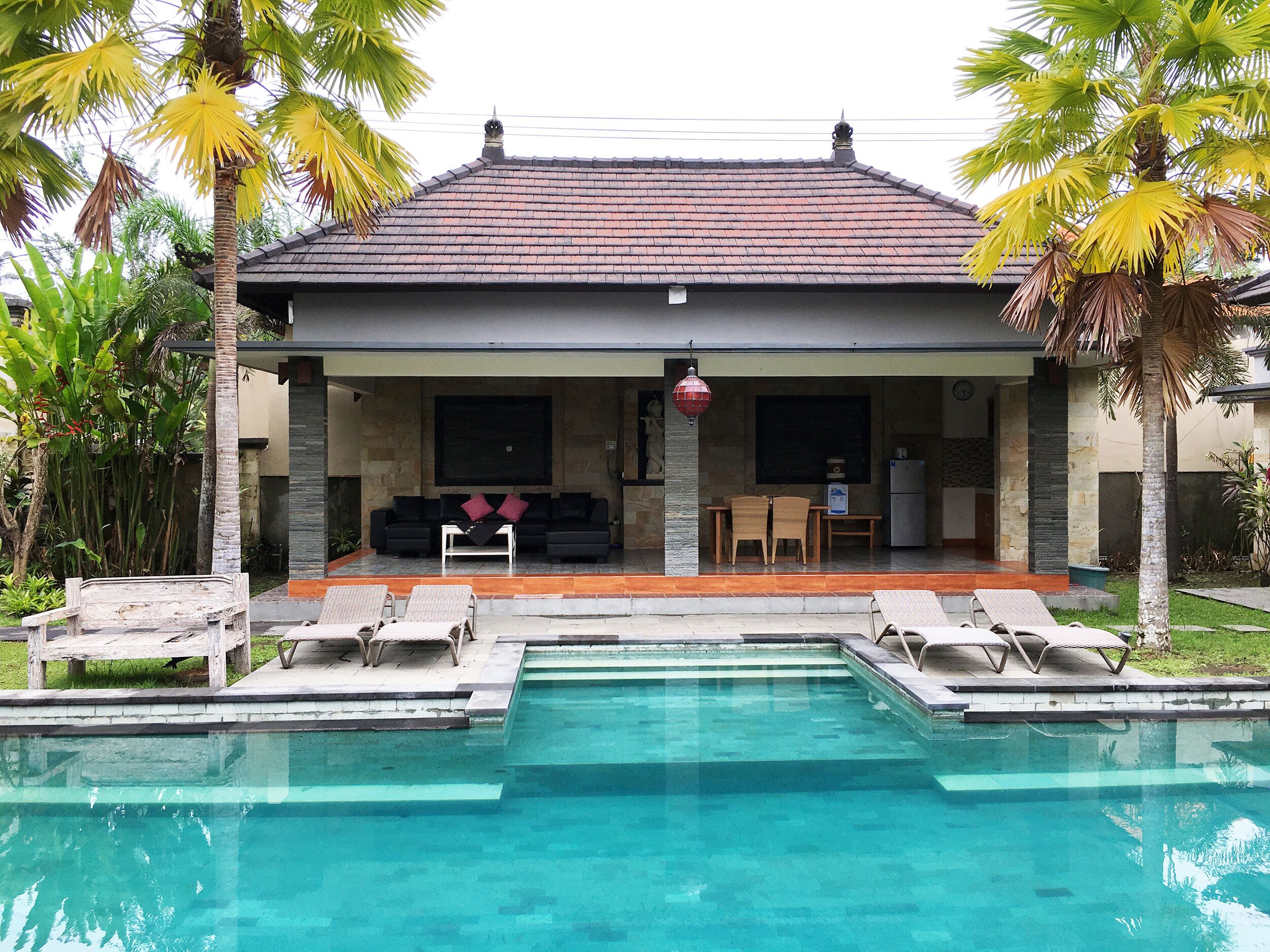 A house with a swimming pool, outdoor seating, and palm trees.