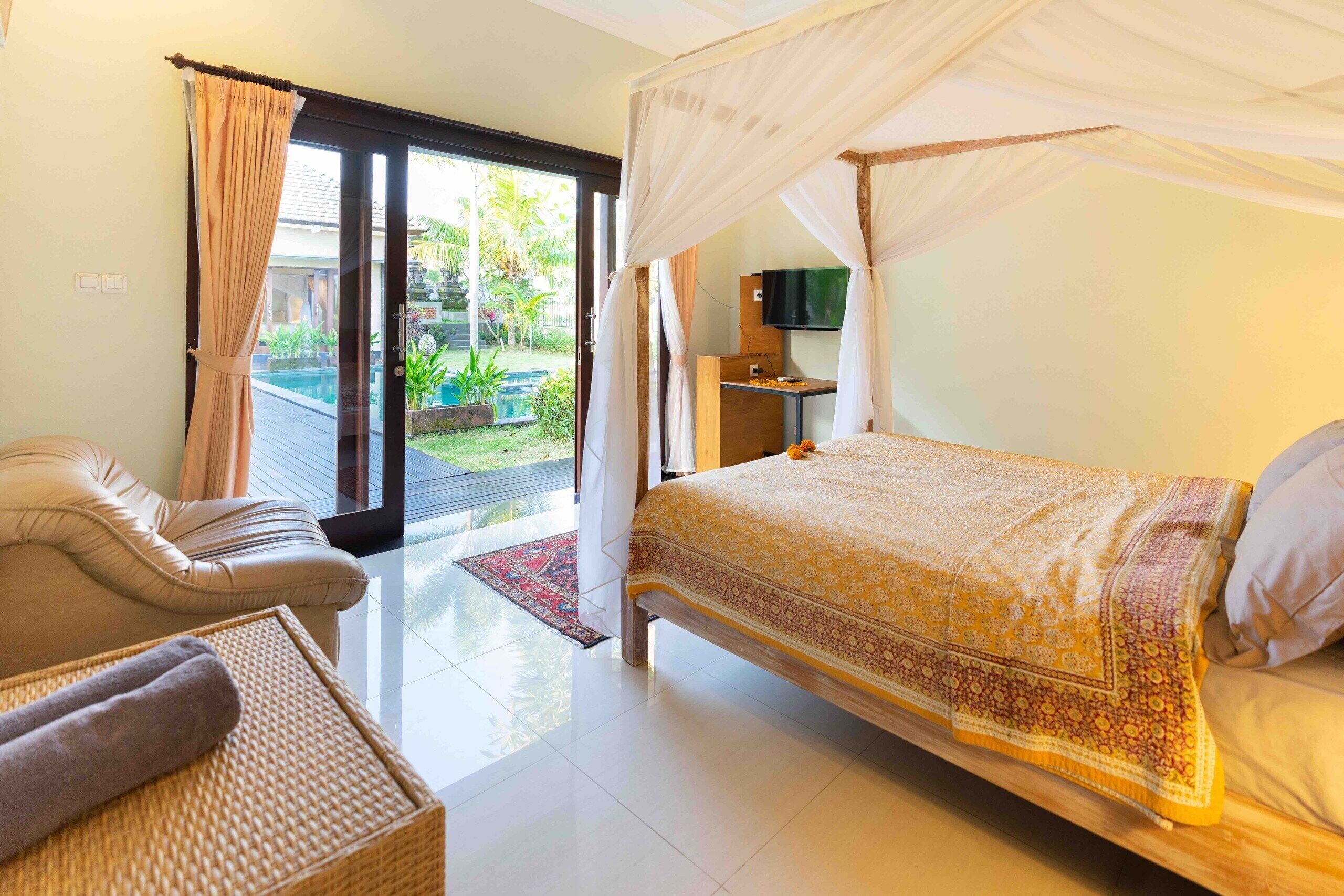 A bedroom with a bed, a sofa, a TV, and a view of a garden.