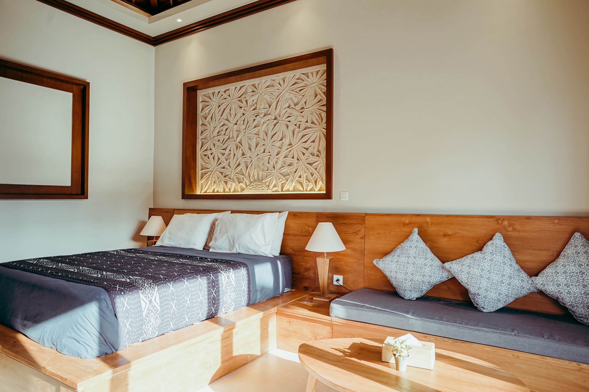 A hotel room with a bed, a sofa, a wooden coffee table, and a decorative wall panel.