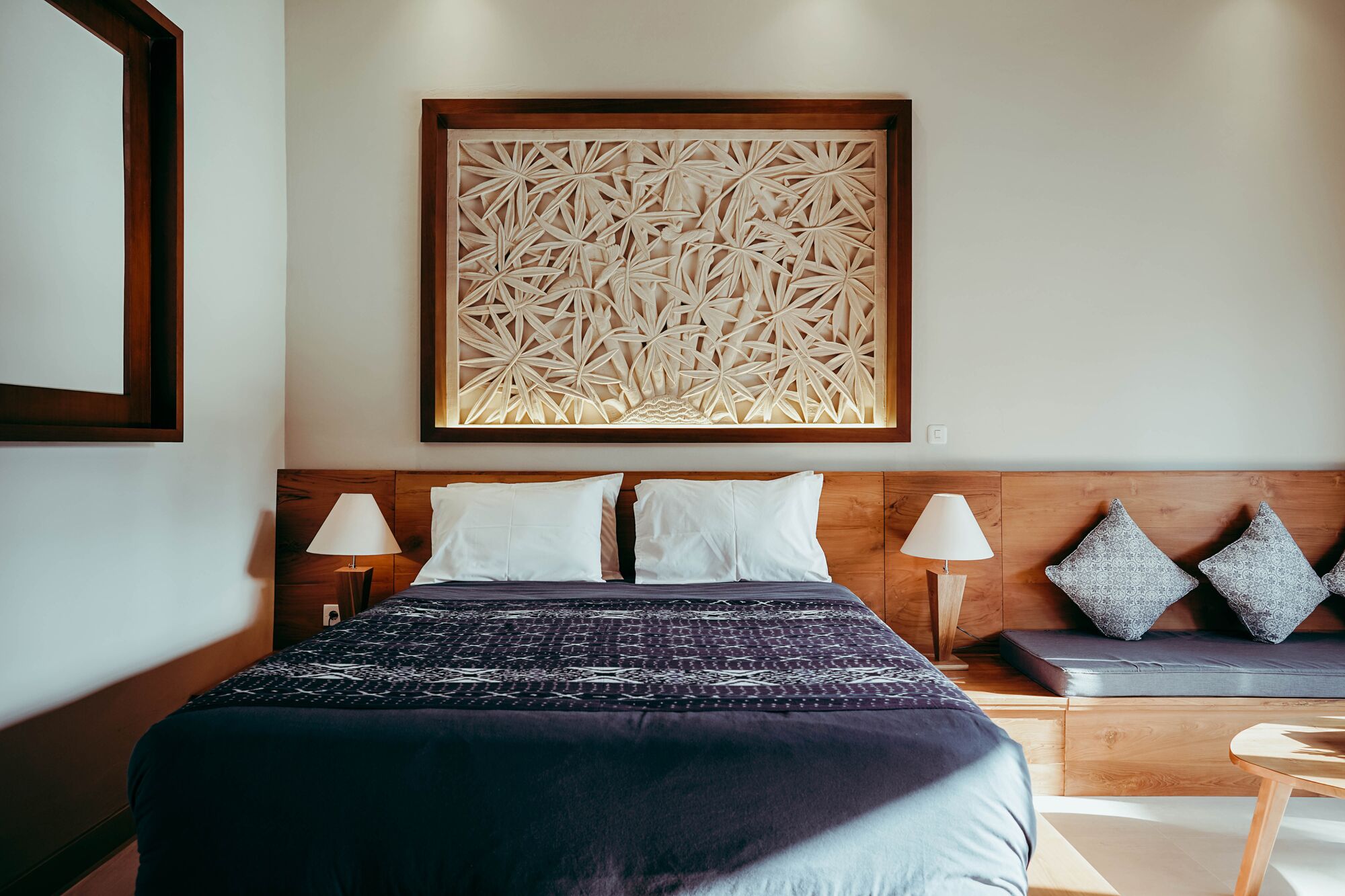 A hotel room with a large bed, two bedside lamps, a wooden headboard, and a decorative wall panel.