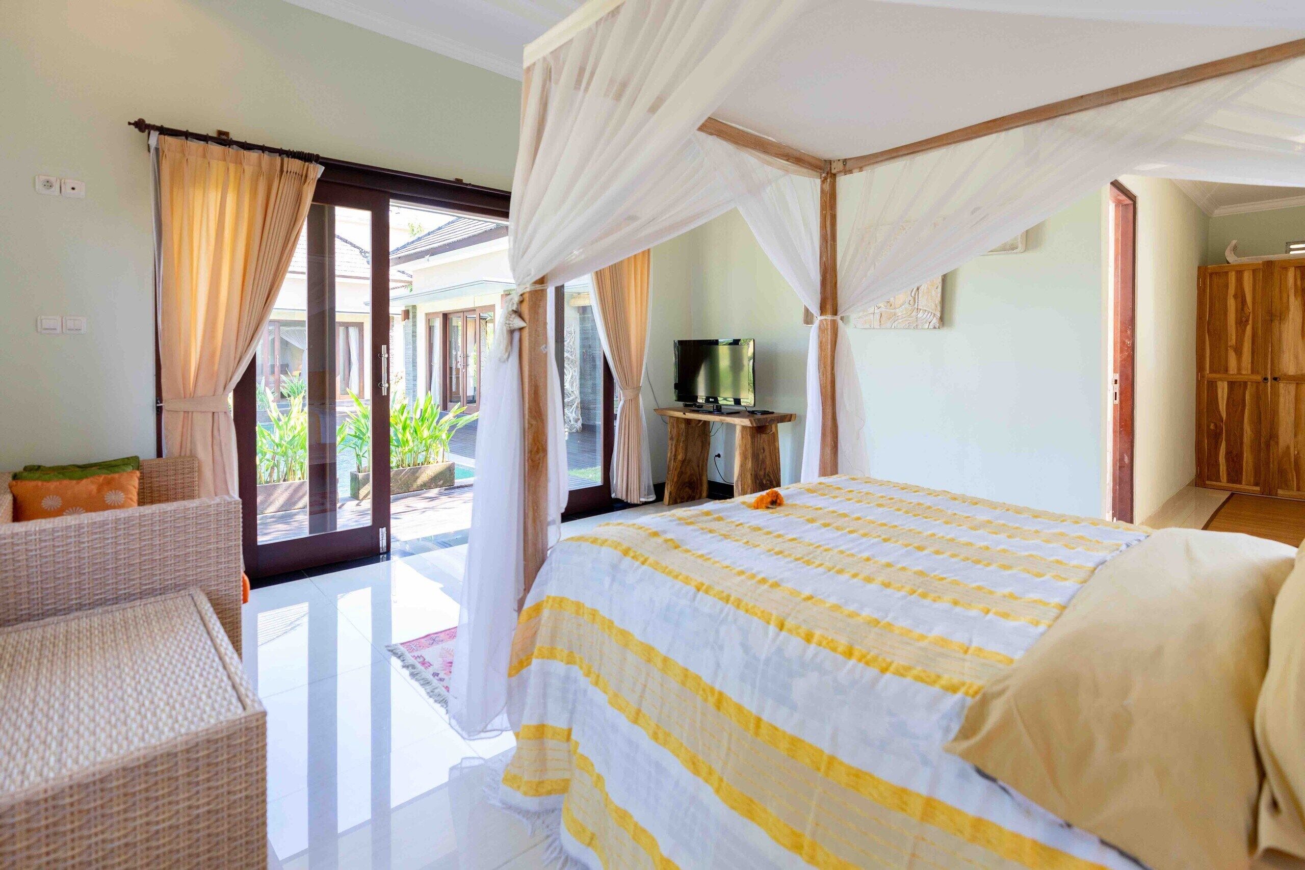 A bedroom with a canopy bed, a television on a wooden stand, and a view of the outdoors through a glass door.
