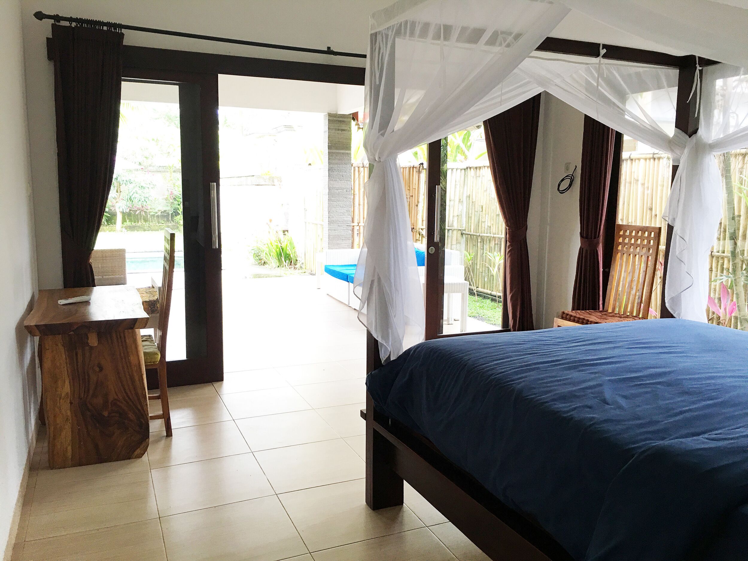 A bedroom with a bed, a desk, and a chair, with a view of the outside.