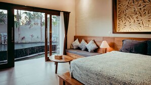 Une chambre d’hôtel comprenant un lit, une table de chevet, une lampe, un canapé avec des coussins, un panneau décoratif mural et une porte-fenêtre coulissante donnant sur un espace extérieur.