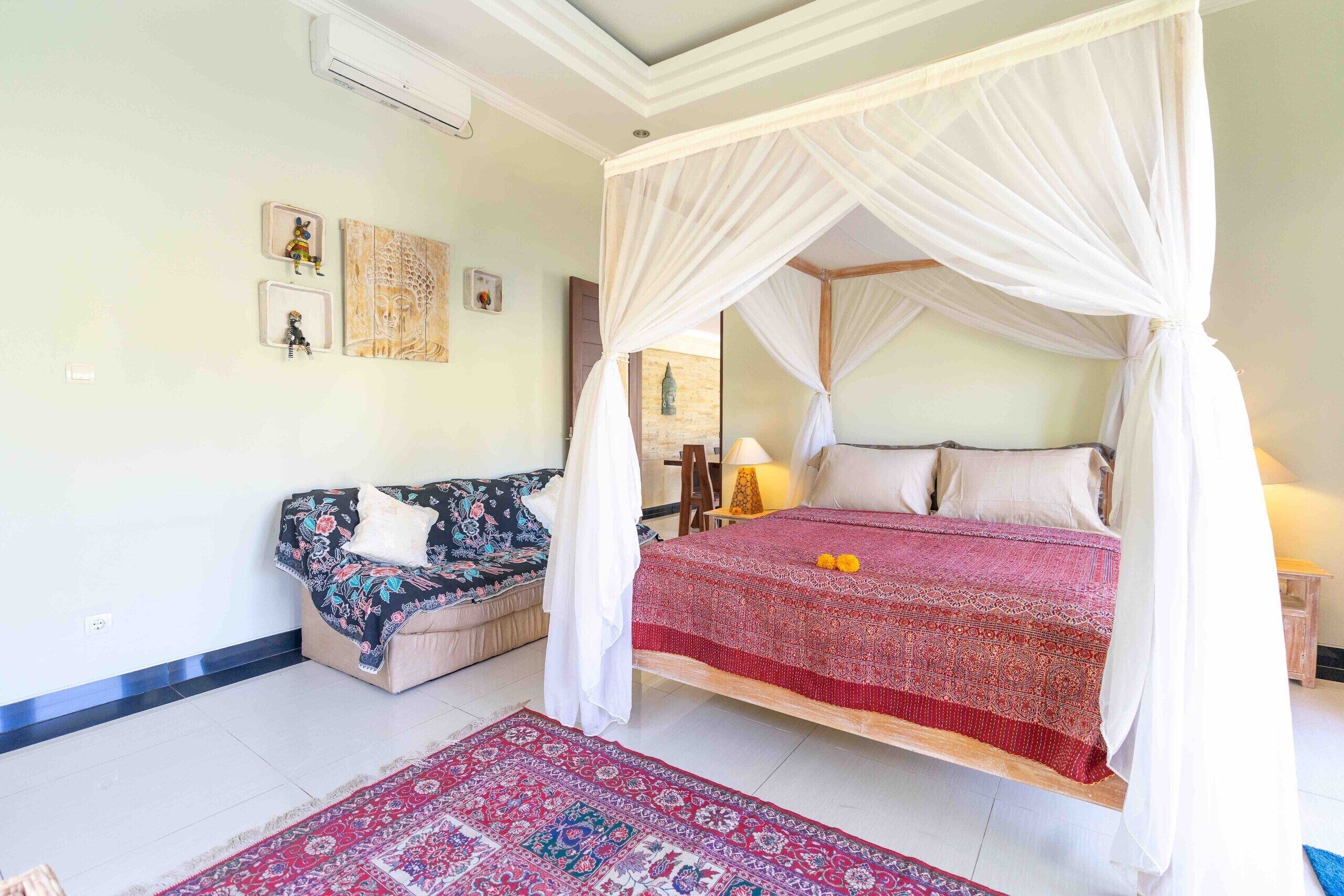A bedroom with a canopy bed, a sofa, and a patterned rug.