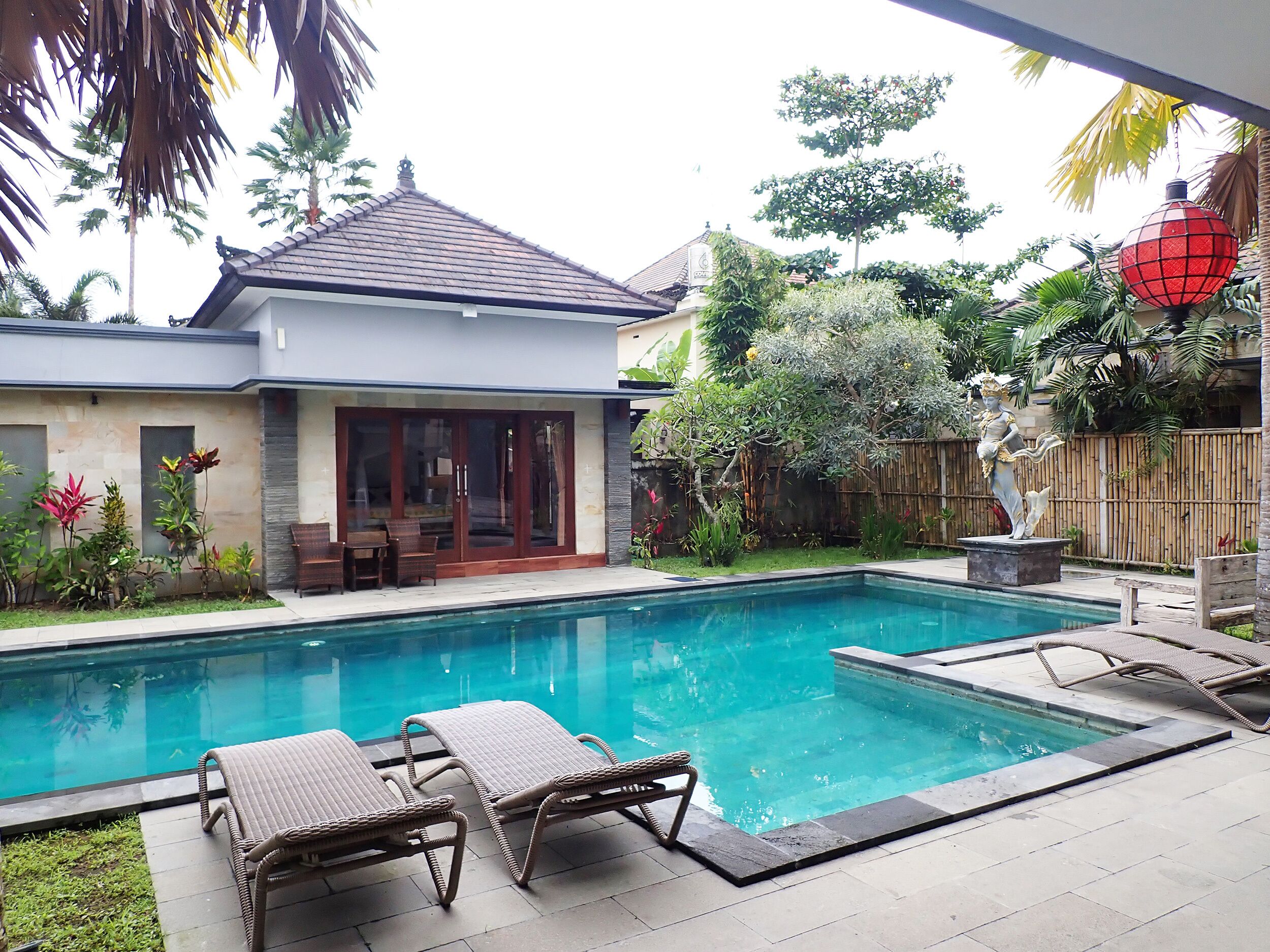 A swimming pool with lounge chairs, a house with a tiled roof, and a statue in the garden.