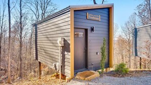 Une petite cabane perchée dans un arbre, d’un seul étage, à l’extérieur sombre, avec une pancarte indiquant : « Cabane dans un pin, propriété de Lumber Jack ».