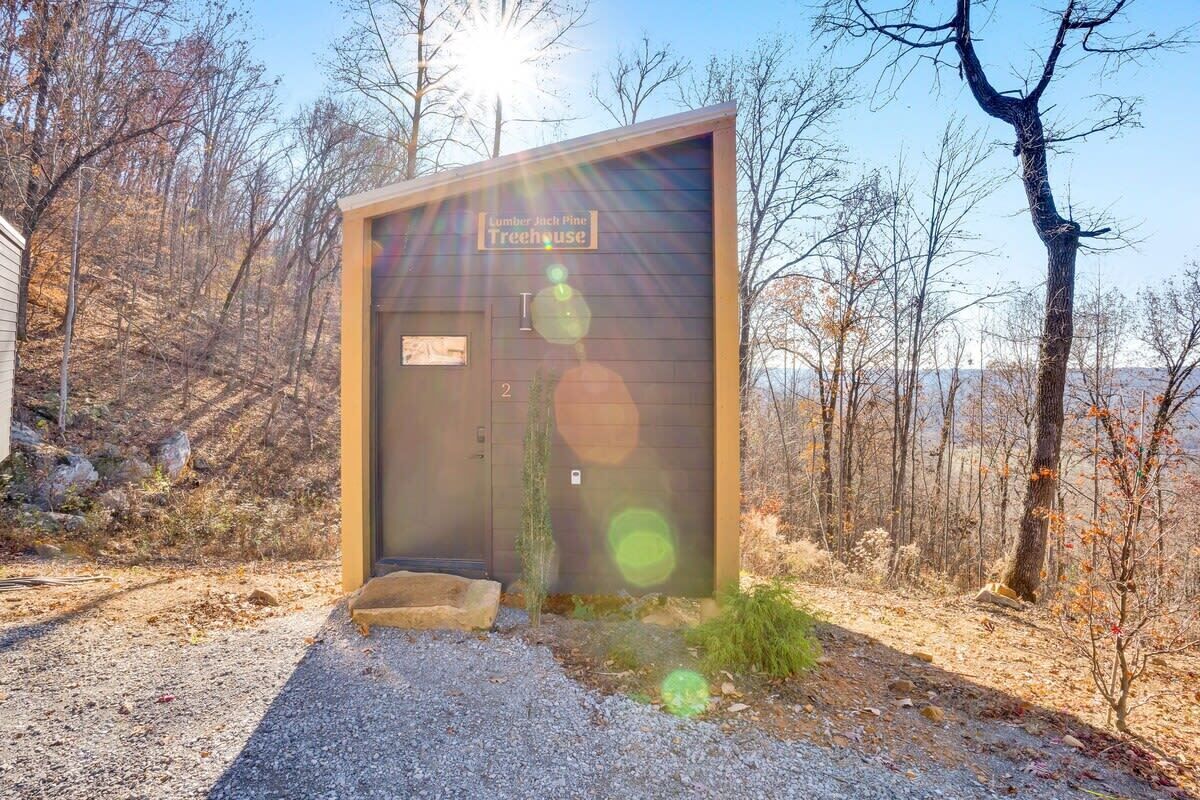 Un edificio pequeño de una sola planta con un letrero que dice "Lumber Jack Pine Treehouse", y un camino de grava que lleva a la entrada.