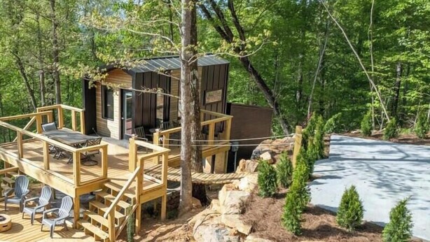 Une cabane dotée d’une terrasse en bois et de meubles de jardin, entourée d’arbres et d’un paysage rocheux.