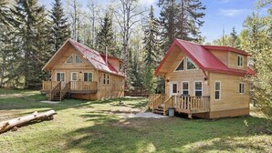 Deux cabanes en bois aux toits rouges, chacune dotée d’un porche à l’avant et d’un escalier menant à l’entrée.