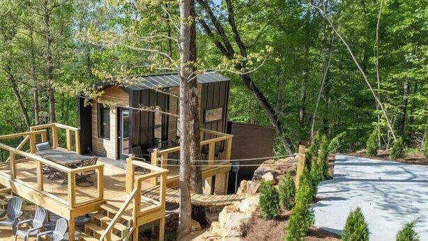 Una cabaña con terraza de madera y asientos al aire libre, rodeada de árboles y un paisaje rocoso.