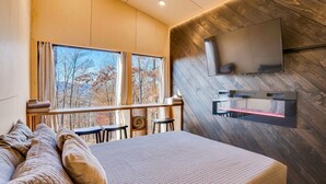 Un dormitorio moderno con una cama grande, un televisor montado en la pared y vistas a árboles por la ventana.