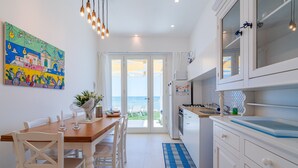 A kitchen with a view to the sea, a dining area with a table and chairs, and a colorful painting on the wall.