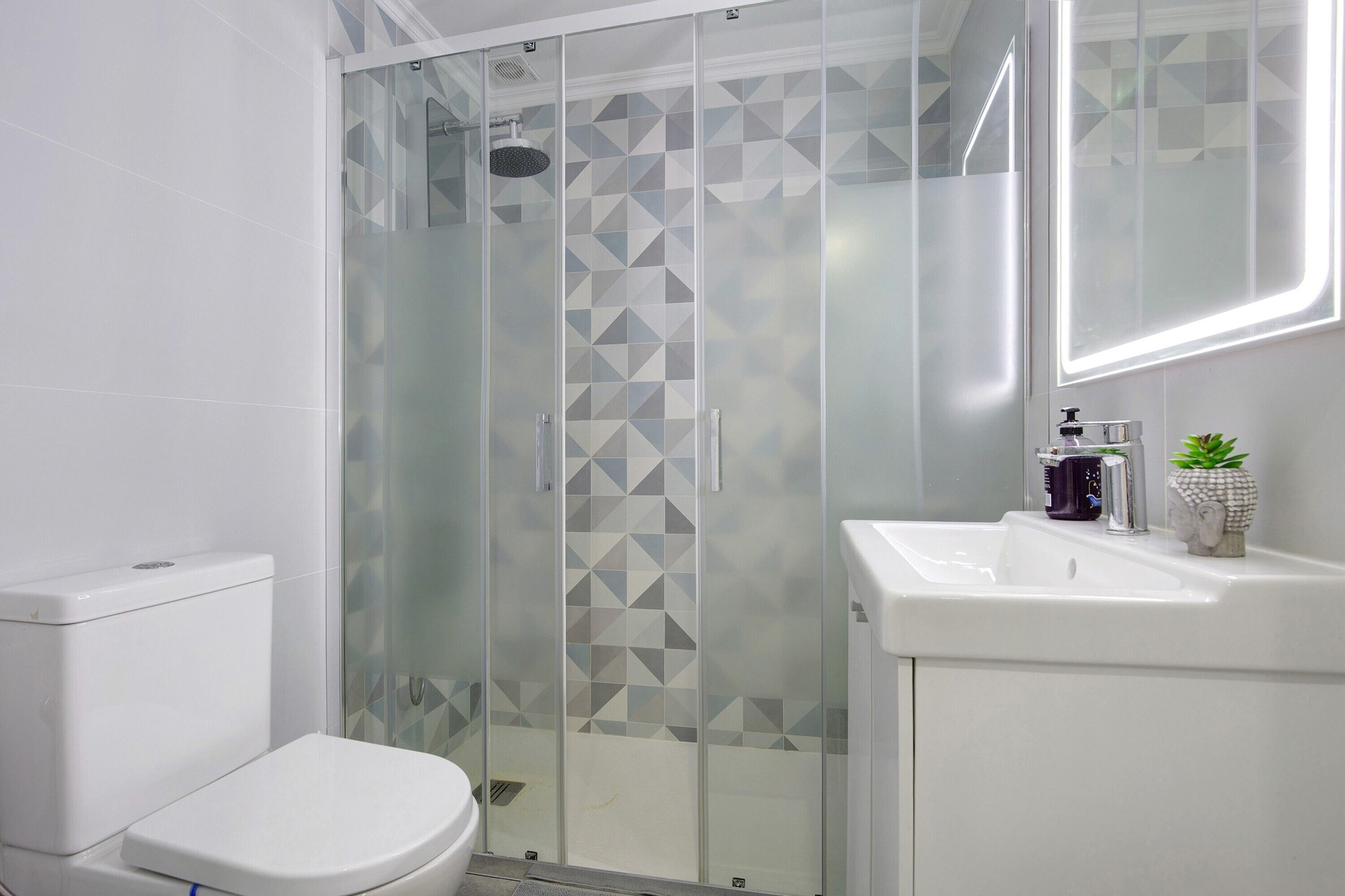 Un baño moderno con cabina de ducha de vidrio, inodoro y lavamanos con espejo.