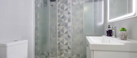 Un baño moderno con cabina de ducha de vidrio, inodoro y lavamanos con espejo.