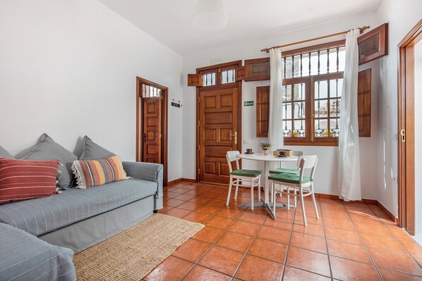 Un salon avec un canapé, une table à manger avec des chaises, une fenêtre avec des rideaux et une porte.