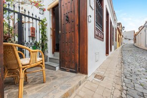 Une rue pavée, une porte en bois, une chaise en osier et un bâtiment blanc avec une clôture en fer noir.
