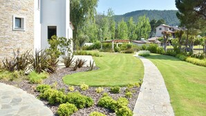 Un edificio de piedra con fachada blanca y techo rojo, rodeado de un jardín cuidado con un camino de piedra que lleva a una pérgola de madera.