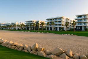 A beachfront hotel with multiple-story buildings, a sandy beach, and palm trees.