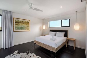 Un dormitorio moderno con una cama grande, un ventilador de techo, un cuadro y una ventana.
