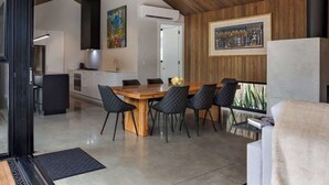 Une cuisine moderne avec un plafond en bois, un coin repas avec une table en bois et des chaises noires, et un grand tableau encadré au mur.