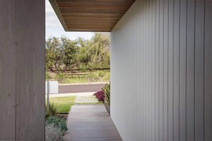 Un corredor exterior cubierto con techo de madera, pared de concreto y un sendero que conduce a una carretera.