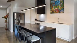 Une cuisine moderne dotée d’un îlot central, d’appareils électroménagers en acier inoxydable et d’une peinture abstraite aux couleurs vives qui orne le mur.