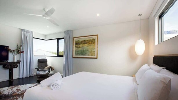Une chambre d’hôtel avec un grand lit, un ventilateur de plafond, un tableau au mur, un bureau avec une chaise et une vue par la fenêtre.