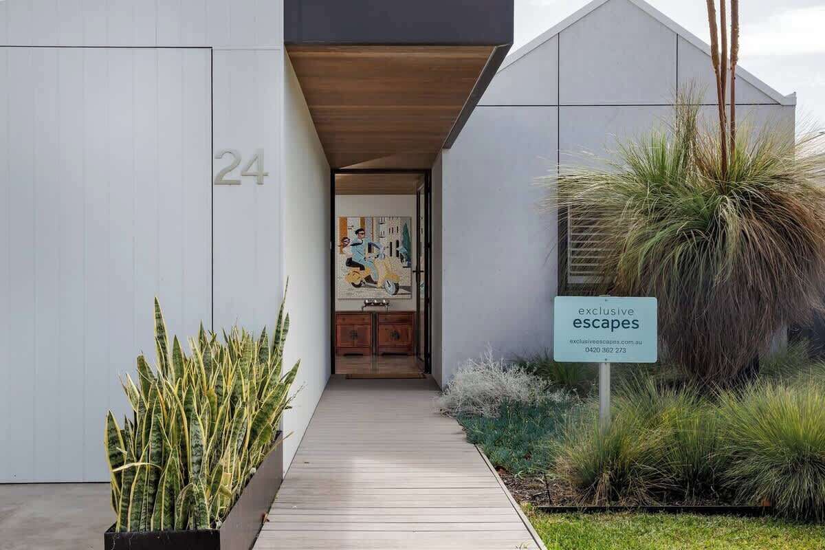 A modern building entrance with a wooden walkway, a number '24' sign, and a sign for 'exclusive escapes.'