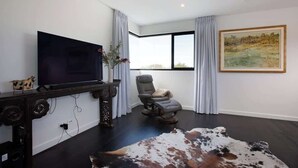 Un salon moderne doté d’un téléviseur à écran plat, d’un canapé en cuir, d’un fauteuil inclinable et d’une grande fenêtre avec des rideaux.