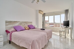 A hotel room with two beds, a TV, a desk, and a large window with a city view. - "Mirador del Mar" Apartment with Sea Views, Shared Pool, and Wi-Fi (Torrox Costa)