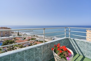 A balcony with a view of the sea, a flower pot, and buildings in the background.