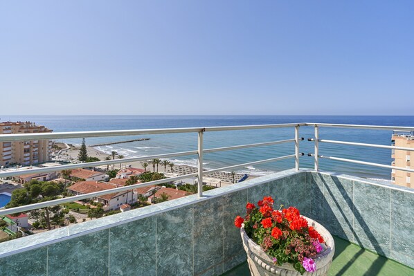 A balcony with a view of the sea, a flower pot, and buildings in the background.