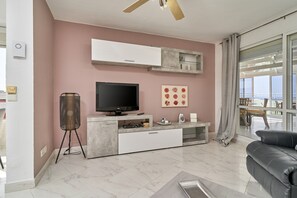A modern living room with a flat-screen TV, a ceiling fan, a large window with a view, and a black leather sofa. - "Mirador del Mar" Apartment with Sea Views, Shared Pool, and Wi-Fi (Torrox Costa)