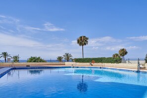 A swimming pool with a clear view of the ocean, surrounded by palm trees and a fence.