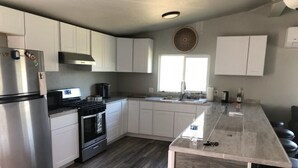 A modern kitchen with white cabinets, stainless steel appliances, a wooden floor, and a bar area with stools.