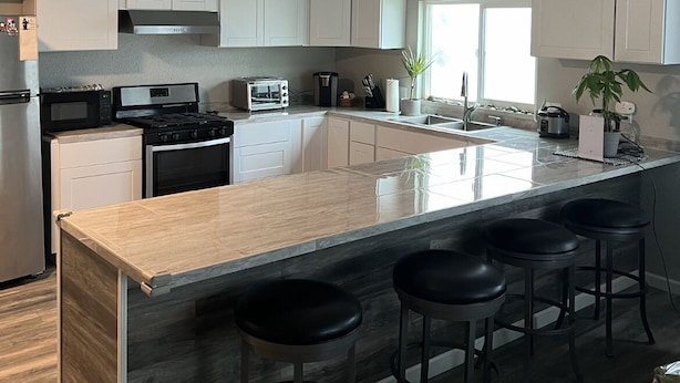 A modern kitchen with white cabinets, a large island with bar stools, a ceiling fan, and a view of the outdoors.