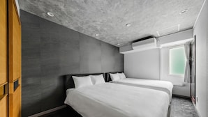 Een moderne hotelkamer met twee bedden, een houten garderobe en een groot raam met gordijnen.