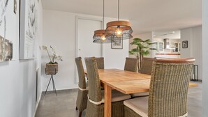 Un coin repas avec une table en bois et des chaises en osier, un luminaire suspendu et une plante en pot.