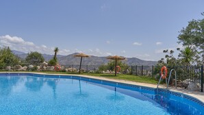 Une piscine à l’eau d’un bleu cristallin, entourée d’une clôture, avec des montagnes en arrière-plan.