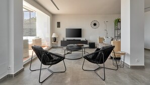 Un salon moderne doté d’un téléviseur à écran plat, de deux fauteuils noirs, d’une table basse ronde et d’une grande fenêtre.