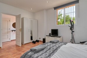 A bedroom with a bed, a TV, a desk, a wardrobe, and a window with a view of greenery. - Holiday Home "Paradiso Tropical" with Sea View, Shared Pool & Wi-Fi (La Herradura (Almunecar))