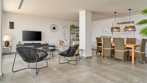 Un salon moderne doté d’un téléviseur à écran plat, de fauteuils en rotin noir, d’une table à manger avec des chaises en rotin et de luminaires suspendus.