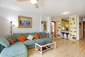 A living room with a sofa, a coffee table, and a kitchen area visible through an open doorway.