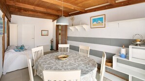 Een eetgedeelte met een ronde tafel, witte stoelen, een hanglamp en een wandplank met een kaars en een kom.